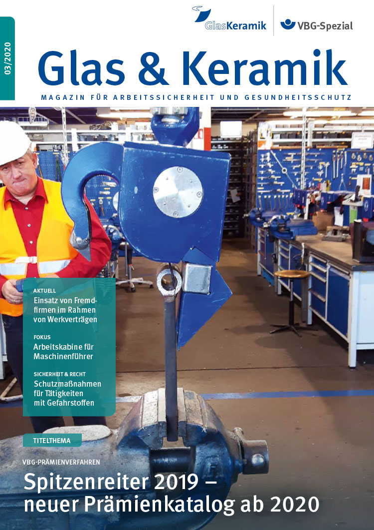 Magazin-Cover: Ein Mann mit Helm und Schutzkleidung bedient mit einer Fernbedienung einen großen blauen Kranhaken, der zu Versuchszwecken an einem Stück Metall in einem großen Schraubstock zieht.