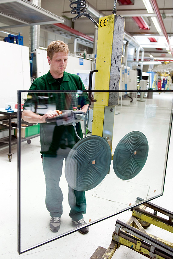 Arbeiter bewegt eine Flachglasscheibe mit Hilfe einer Vakuumhebeeinrichtung.