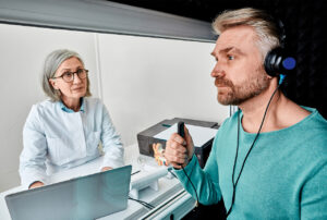 Ein Mann bei einer audiometrischen Prüfung, überwacht von medizinischem Personal