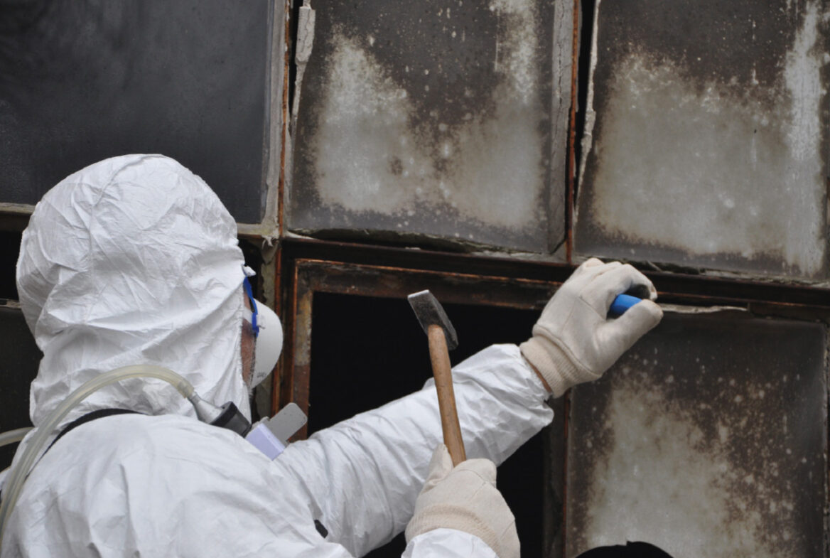 Ein Mitarbeiter in Schutzkleidung und Atemschutz beim Enfernen von altem Kit aus einem Glasfalz