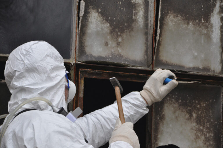 Ein Mitarbeiter in Schutzkleidung und Atemschutz beim Enfernen von altem Kit aus einem Glasfalz